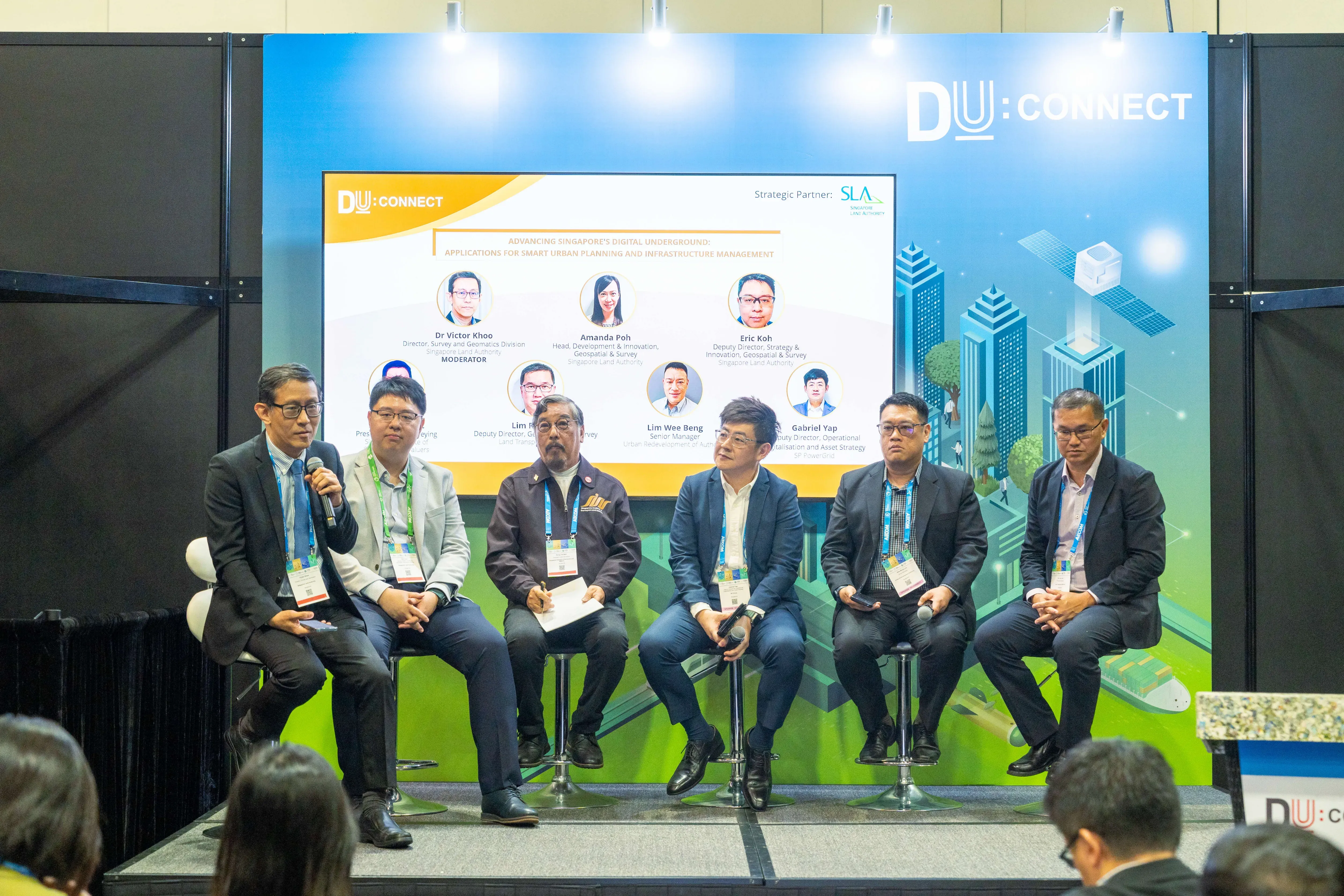 Six panelists seated on stools at a DU:CONNECT event stage, one speaking into a microphone.